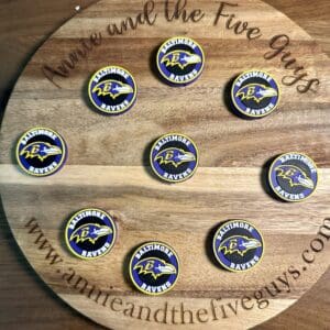 A wooden board with the words "Annie and the Five Guys" displaying eight Baltimore Football Silicone Focal Beads, each featuring the Ravens logo.