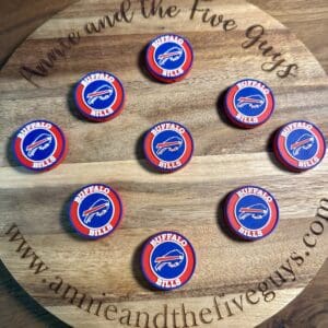 A wooden board featuring "www.annieandthefiveguys.com" with nine round tokens adorned with Buffalo-themed silicone focal beads.