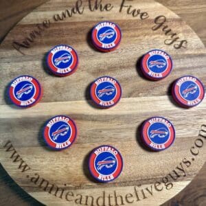 A wooden board featuring "www.annieandthefiveguys.com" with nine round tokens adorned with Buffalo-themed silicone focal beads.