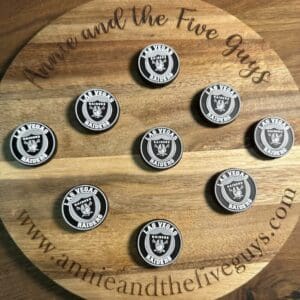 A round wooden board with "Annie and the Five Guys" text displays nine Las Vegas football silicone focal beads, arranged in a grid. The website "www.annieandthefiveguys.com" is visible on the board.