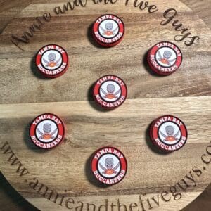 Seven Tampa Bay Buccaneers bottle caps arranged on a circular wooden board engraved with text and a website URL.