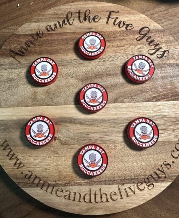 Seven Tampa Bay Buccaneers bottle caps arranged on a circular wooden board engraved with text and a website URL.