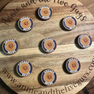 Wooden board displaying nine Chicago football silicone focal beads arranged in a 3x3 grid with the website "annieandthefiveguys.com" inscribed around the edge.