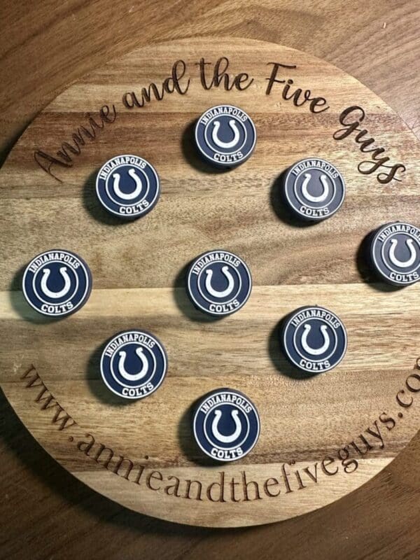 A round wooden board featuring the text "Annie and the Five Guys," adorned with nine circular pins representing the Indianapolis Colts.