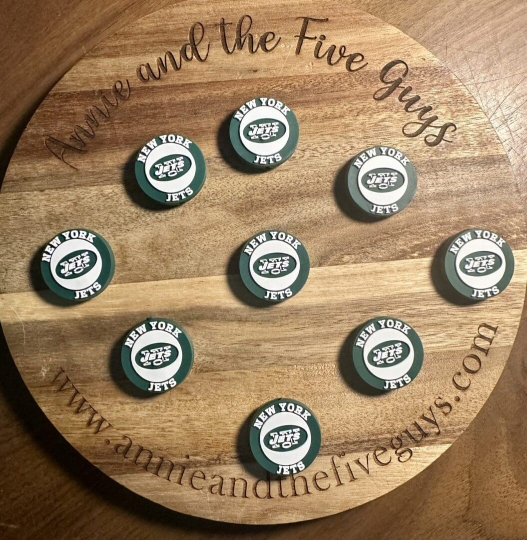 A wooden board featuring nine New York Football Silicone Focal Beads arranged in a grid. The board is engraved with "Annie and the Five Guys" and a website URL.