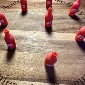 Red bottle-shaped objects arranged in a circular pattern on a wooden surface with engraved text.