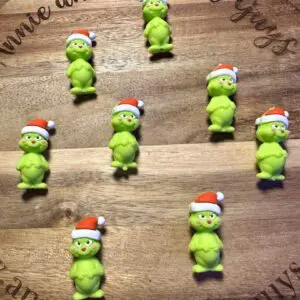 A circular wooden board with "Annie and the Five Guys" engraved holds eight green Grinch-themed treats decorated with Santa hats.