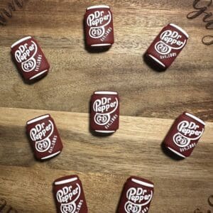 Nine Dr Pepper-themed erasers arranged in a circle on a wooden surface.