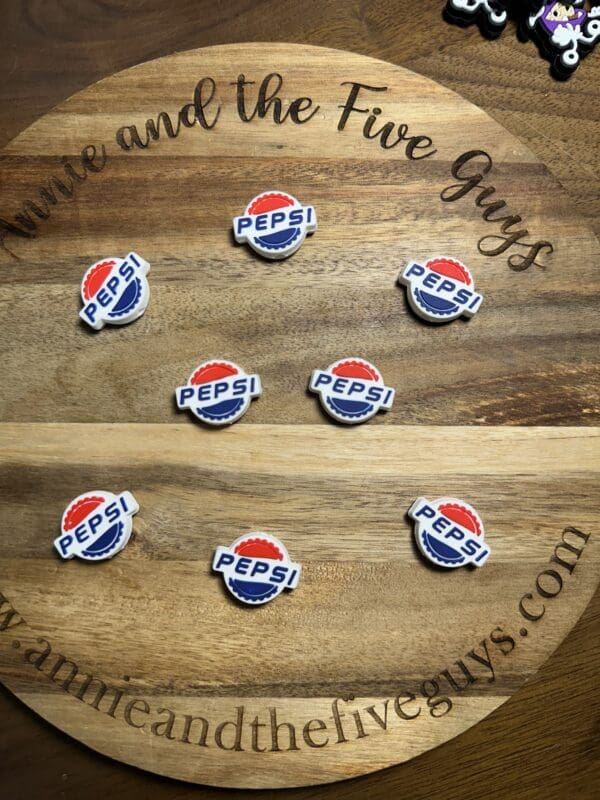 Seven Pepsi bottle cap magnets arranged on a round wooden surface with "Annie and the Five Guys" engraved.