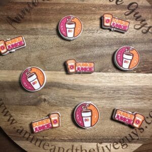 A wooden board displays nine Dunkin' coffee-themed decorative pins arranged in a circle.