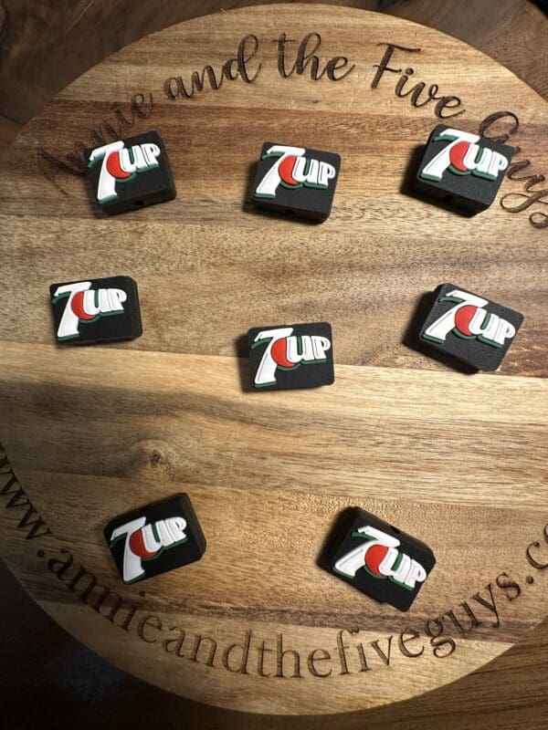 Seven black drink coasters with the 7UP logo are arranged on a wooden surface displaying the text "www.annmeandthefiveguys.com" around the edge.