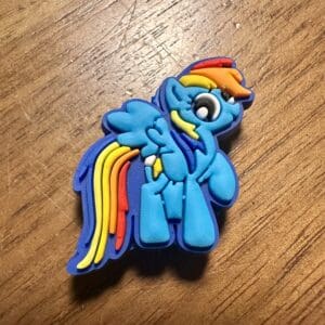 A blue cartoon pony with a rainbow mane and tail is depicted on a wooden surface.