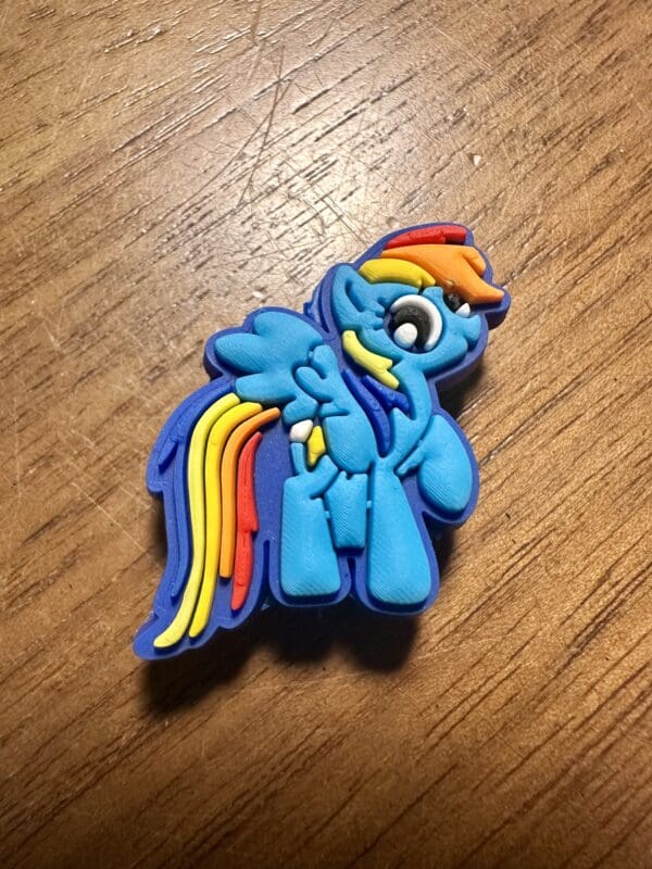 A blue cartoon pony with a rainbow mane and tail is depicted on a wooden surface.