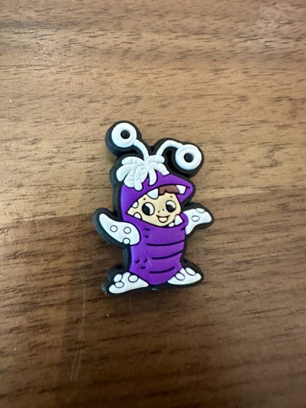 A small cartoon character in a purple bug costume with white wings and antennae on a wooden surface.