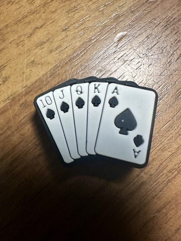 A hand of poker cards in black spades suit displaying a royal flush: 10, Jack, Queen, King, and Ace on a wooden surface.