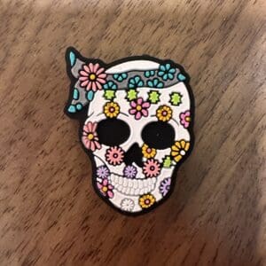 A skull pin decorated with colorful flowers on a wooden surface.