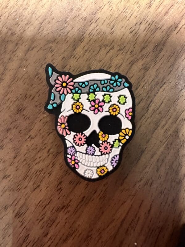 A skull pin decorated with colorful flowers on a wooden surface.