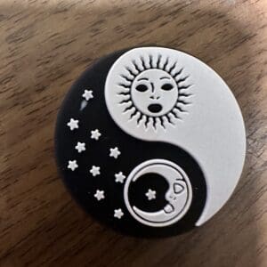 A yin-yang symbol with a sun in the black half and a moon with stars in the white half, set against a wooden surface.