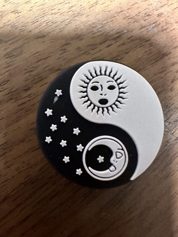 A yin-yang symbol with a sun in the black half and a moon with stars in the white half, set against a wooden surface.