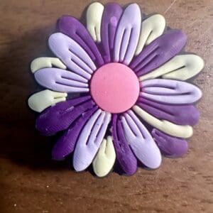 A colorful clay flower with pink, purple, and light green petals on a wooden surface.