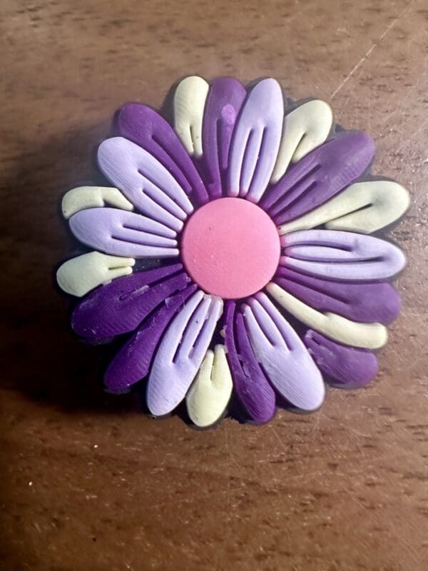 A colorful clay flower with pink, purple, and light green petals on a wooden surface.