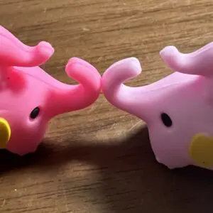 Two small, pink plastic elephant figurines with yellow accents face each other on a wooden surface.