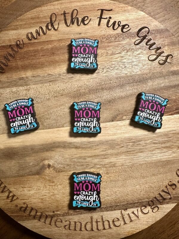 Five identical decorative magnets on a wooden board, each with the phrase "Tough enough to be a Mom, crazy enough to love it.