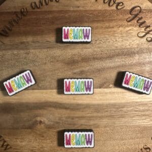 Five colorful "MEMAW" pins arranged on a wooden surface.