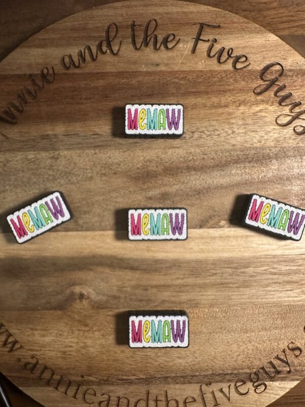 Five colorful "MEMAW" pins arranged on a wooden surface.