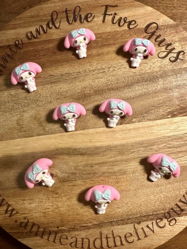 Nine pink and white bunny-shaped pins with blue bows are arranged in rows on a wooden board that is engraved with "annie and the five guys.