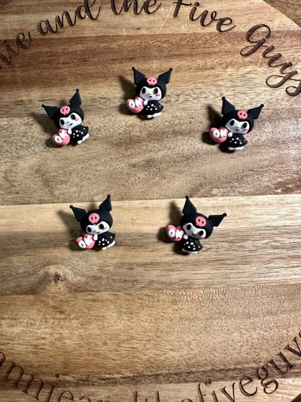 Five small pig-shaped decorations wearing black outfits, arranged on a wooden surface.