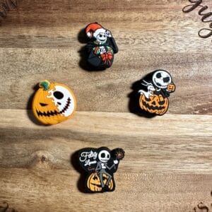 Four Jack Skellington-themed pins on a wooden surface, featuring Halloween designs with pumpkins and festive elements.