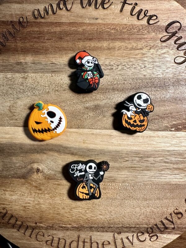 Four Jack Skellington-themed pins on a wooden surface, featuring Halloween designs with pumpkins and festive elements.