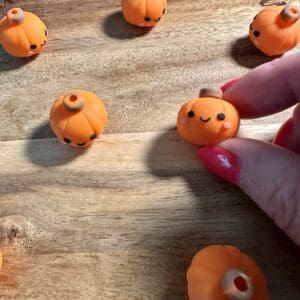 Hand holding a small orange pumpkin with a cute face, placed on a wooden surface with other similar pumpkins.