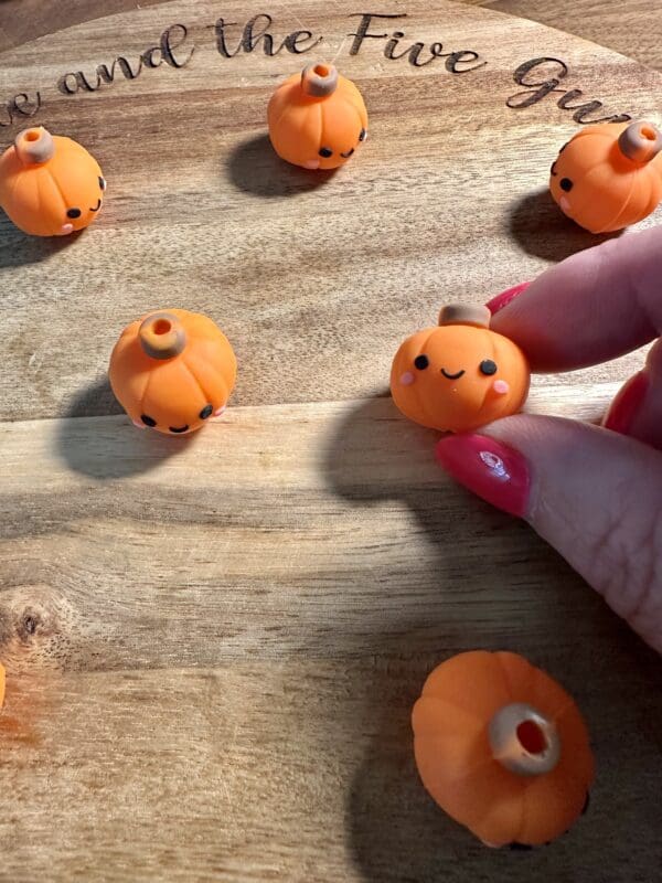 Hand holding a small orange pumpkin with a cute face, placed on a wooden surface with other similar pumpkins.