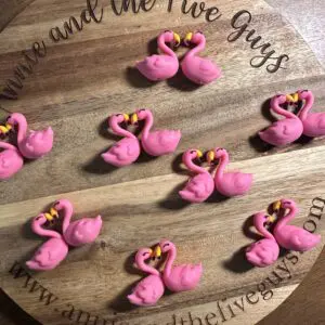 Pink flamingo-shaped decorations arranged on a wooden tray with engraved text, "Annie and the Five Guys.