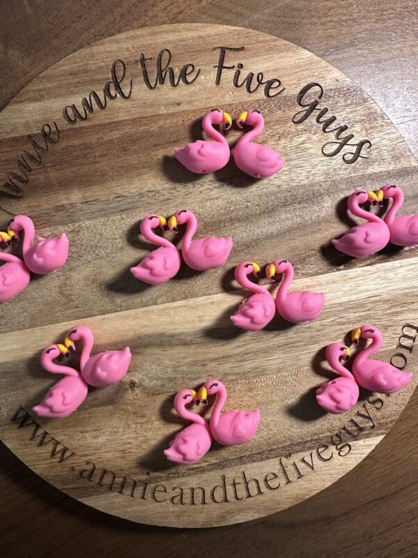 Pink flamingo-shaped decorations arranged on a wooden tray with engraved text, "Annie and the Five Guys.