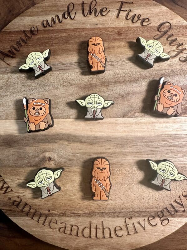 Wooden board displaying various wooden pins shaped like sci-fi characters with an engraved website link.