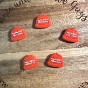 Five small red hats with "Make America Great Again" text on a wooden board with engraved text.