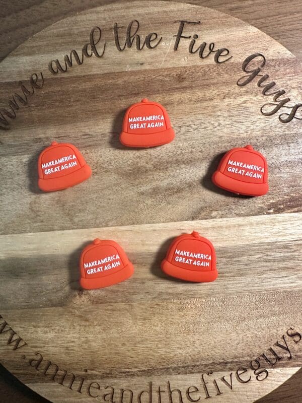 Five small red hats with "Make America Great Again" text on a wooden board with engraved text.