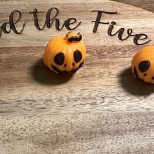 Three pumpkin-shaped orange chocolates with smiling faces on a wooden surface with partially visible lettering.