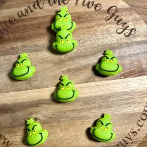 Six green Grinch face buttons arranged on a wooden board with engraved text.