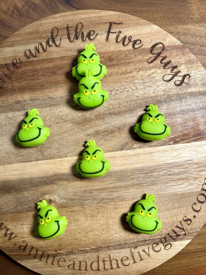 Six green Grinch face buttons arranged on a wooden board with engraved text.