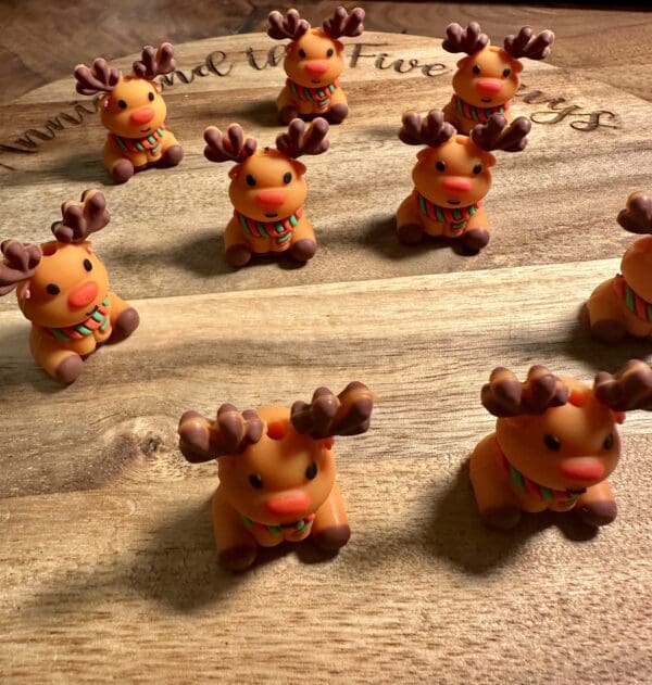 Clay reindeer figurines with scarves are arranged on a wooden surface.