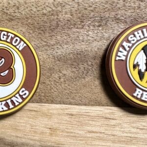 Two circular Washington Redskins logos on a wooden surface. One features a stylized "R" and the other shows a Native American profile.