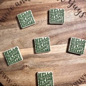 Six square cookies with green text saying "Hello, I'm your husband's favorite husband" are arranged on a wooden board engraved with "Annie and the Five Guys.