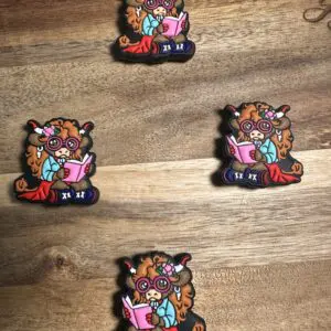 Four identical pins featuring a cartoon character with glasses, horns, and a floral headband, sitting with a book, on a wooden surface.