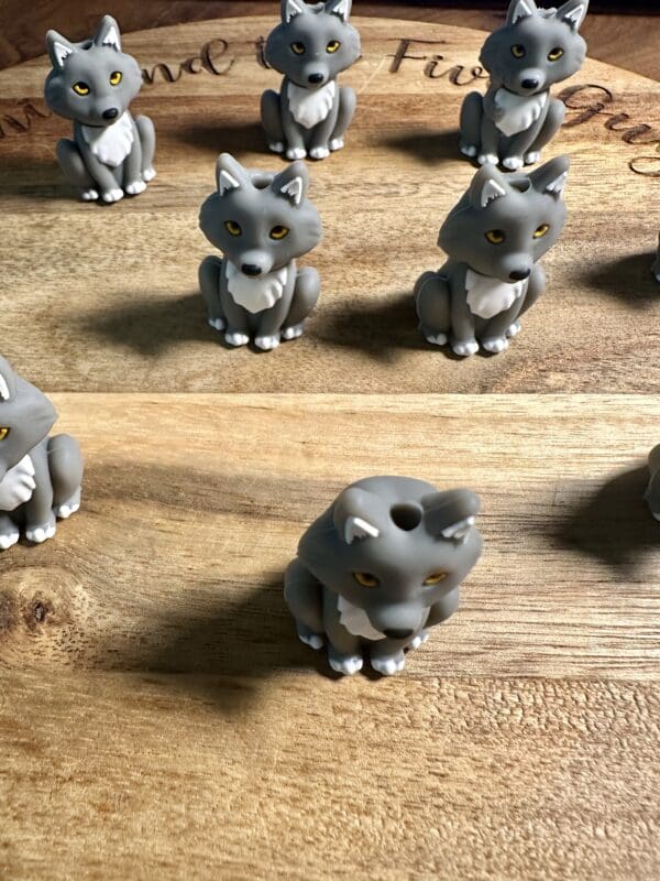 Several small, gray wolf figurines with white accents and yellow eyes are arranged on a wooden surface.