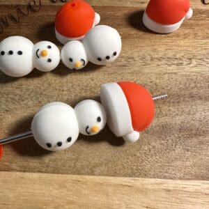 Four snowman-shaped cake toppers with red hats lie on a wooden surface.