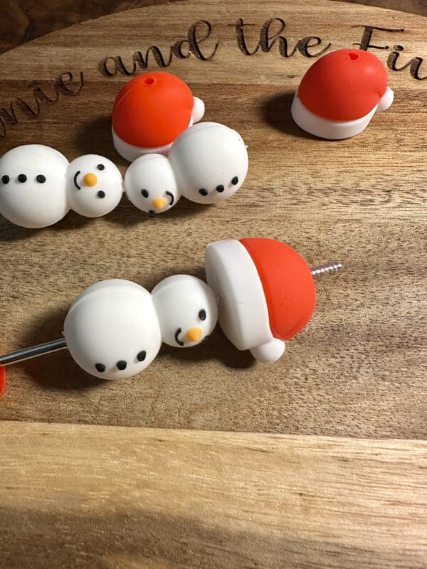 Four snowman-shaped cake toppers with red hats lie on a wooden surface.